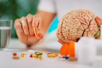 Cognitive improvement or brain supplements. Woman holding a supplement capsule and a model brain.