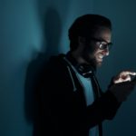 Confident young man smiling while using smart phone in the dark