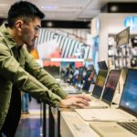Focused ethnic man choosing laptop in shop