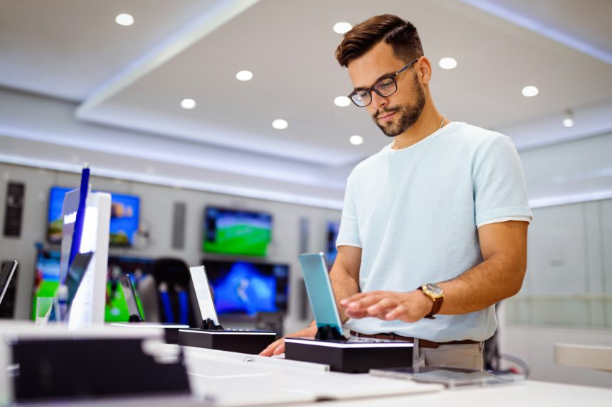 Happy young man trying out new smart phone, digital devices. Tech store interior.